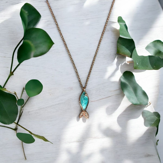 Azure silver fish necklace in rose gold on wooden surface with green leaves.
