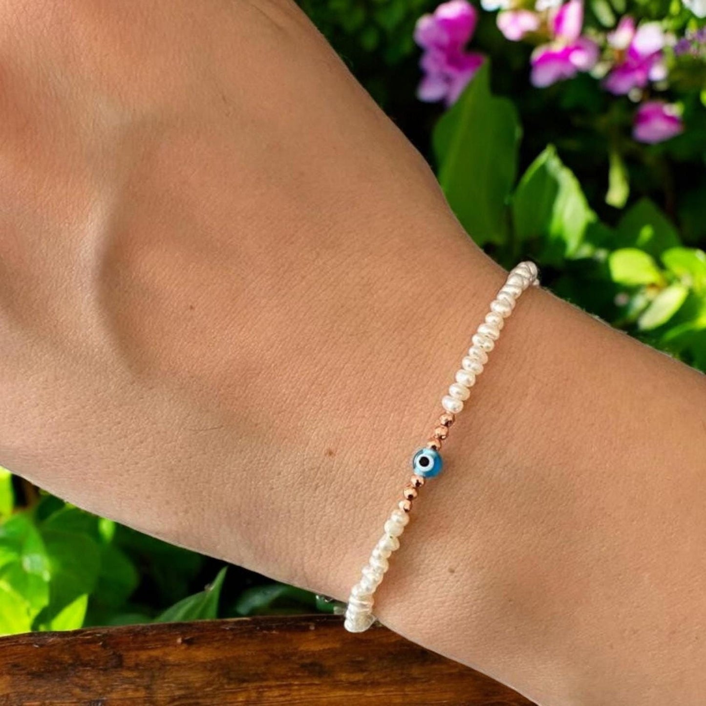Elegant freshwater pearl bracelet featuring a mini evil eye charm, displayed on a wrist against a floral background.