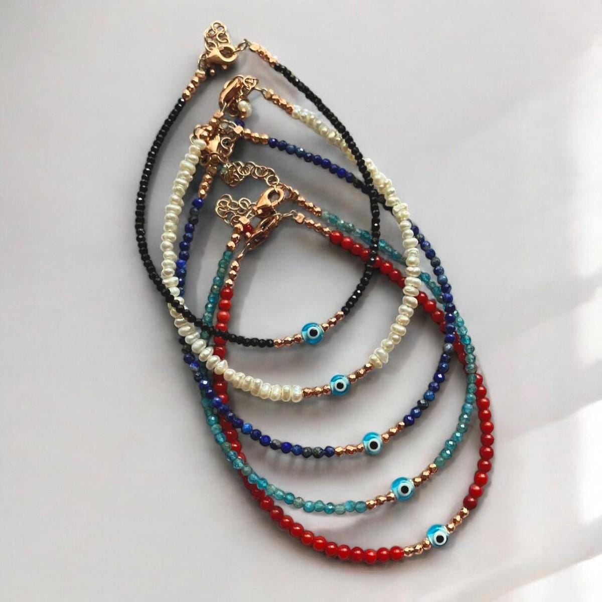 A collection of freshwater pearl bracelets featuring mini evil eye charms in various colours and delicate designs.