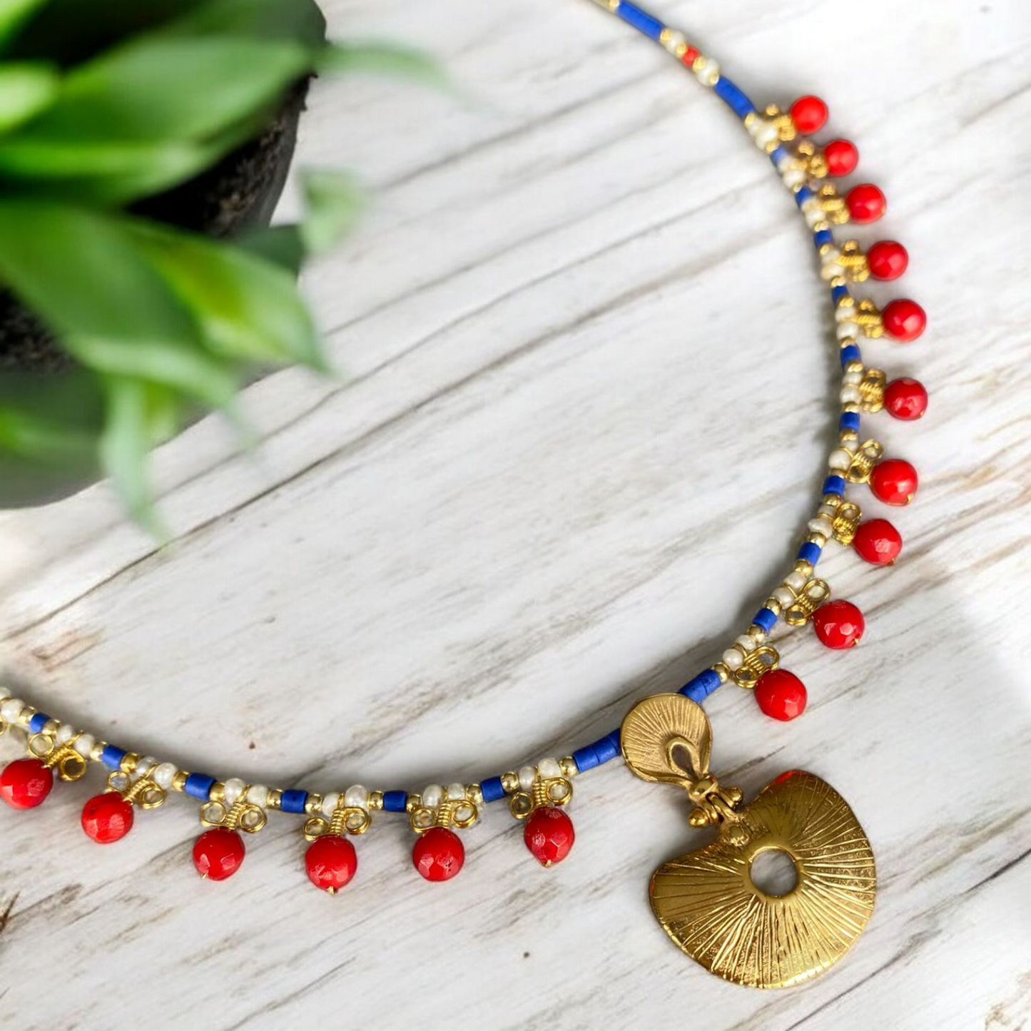 Hera Coral and Lapis Lazuli Gemstone Necklace in 925 Silver with Gold Plating on a white wooden surface, showcasing vibrant red and blue beads with a golden pendant.