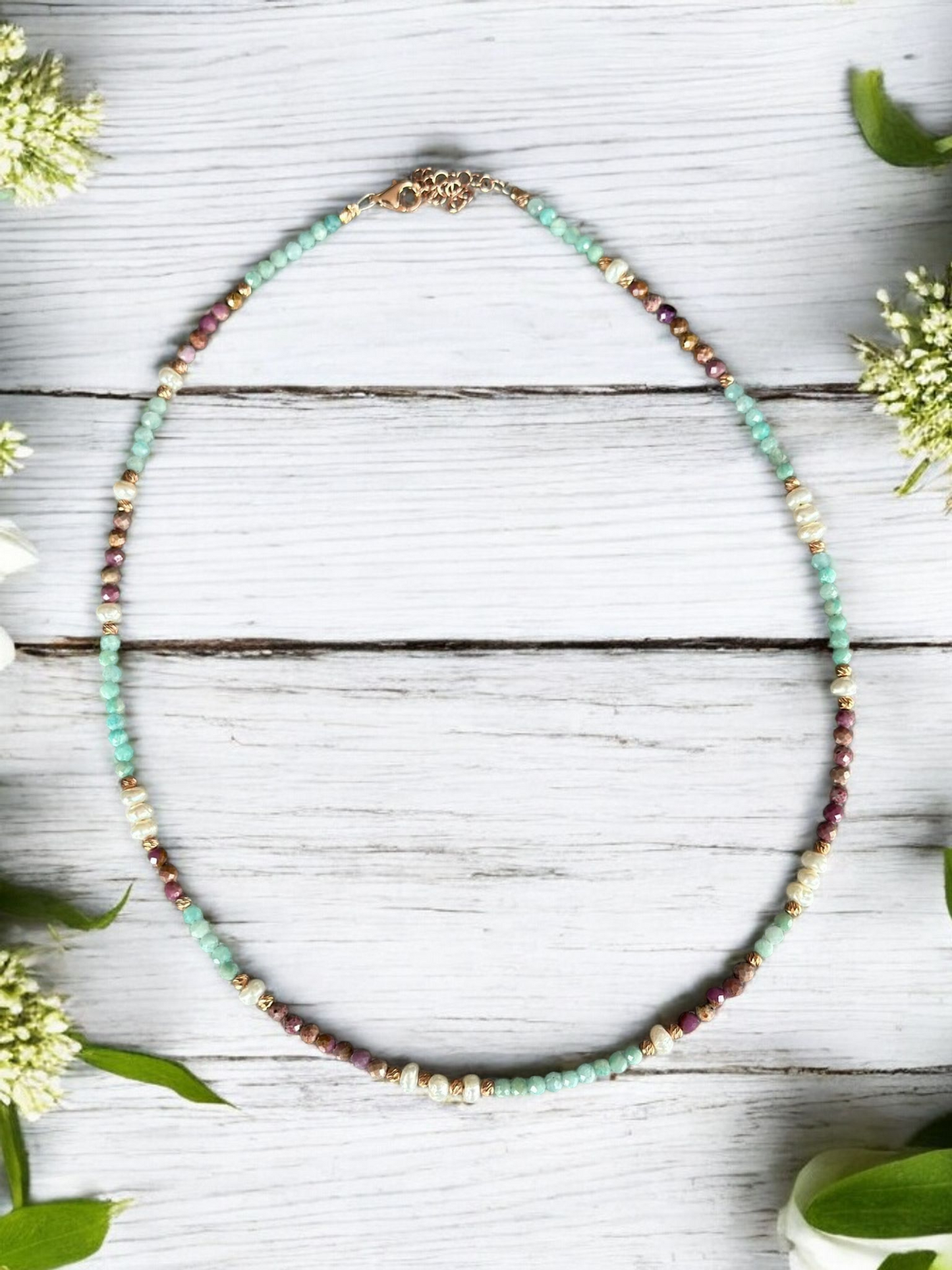 Lilith Gemstone Necklace with Lepidolite, Amazonite, and Freshwater Pearls beautifully arranged on wood with floral accents.