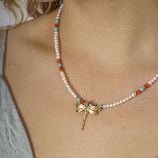 Close-up of a pearl and gemstone necklace featuring a silver dragonfly pendant worn with a green outfit.