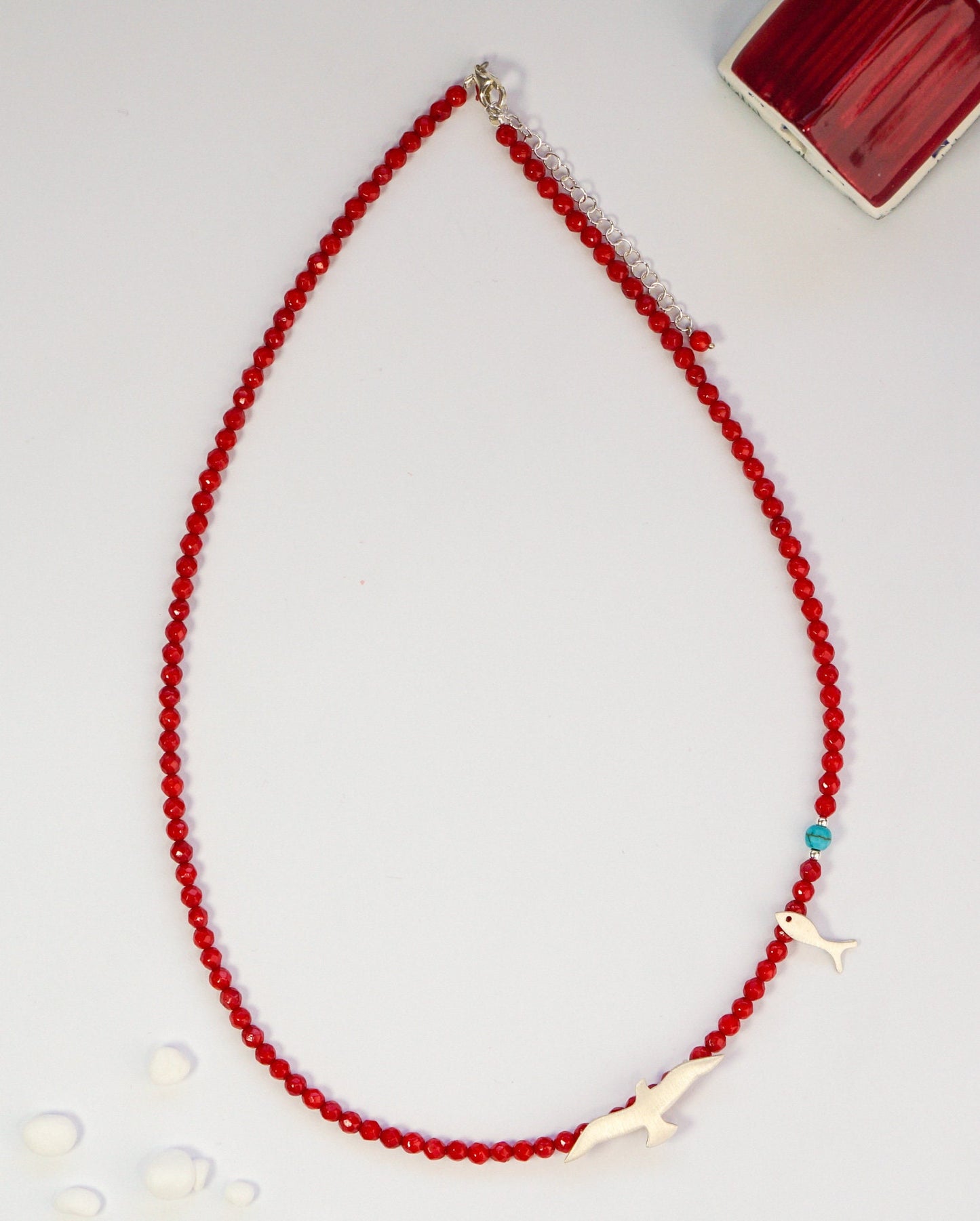 Red coral and silver necklace featuring seagull and fish charms, laid against a light background for a detailed view.