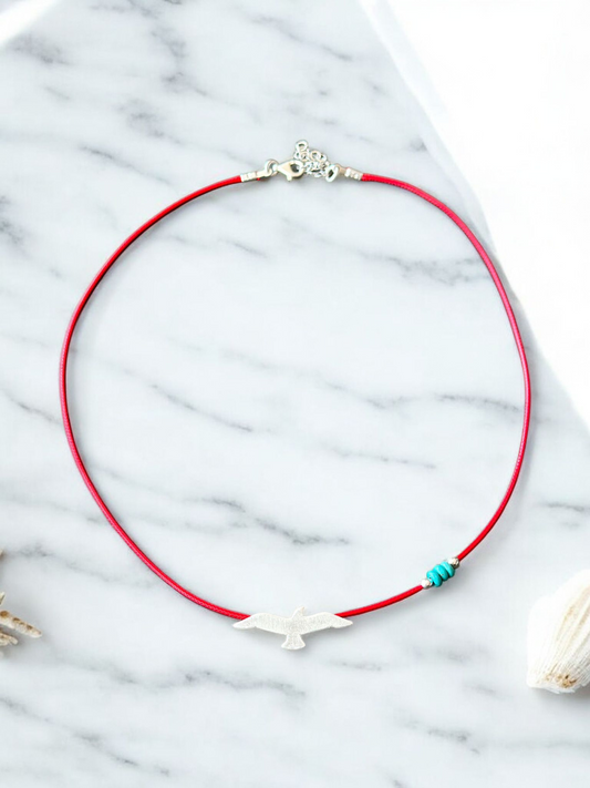 Elegant Silver Seagull Pendant on Red Cord Necklace with Turquoise Beads on Marble Background