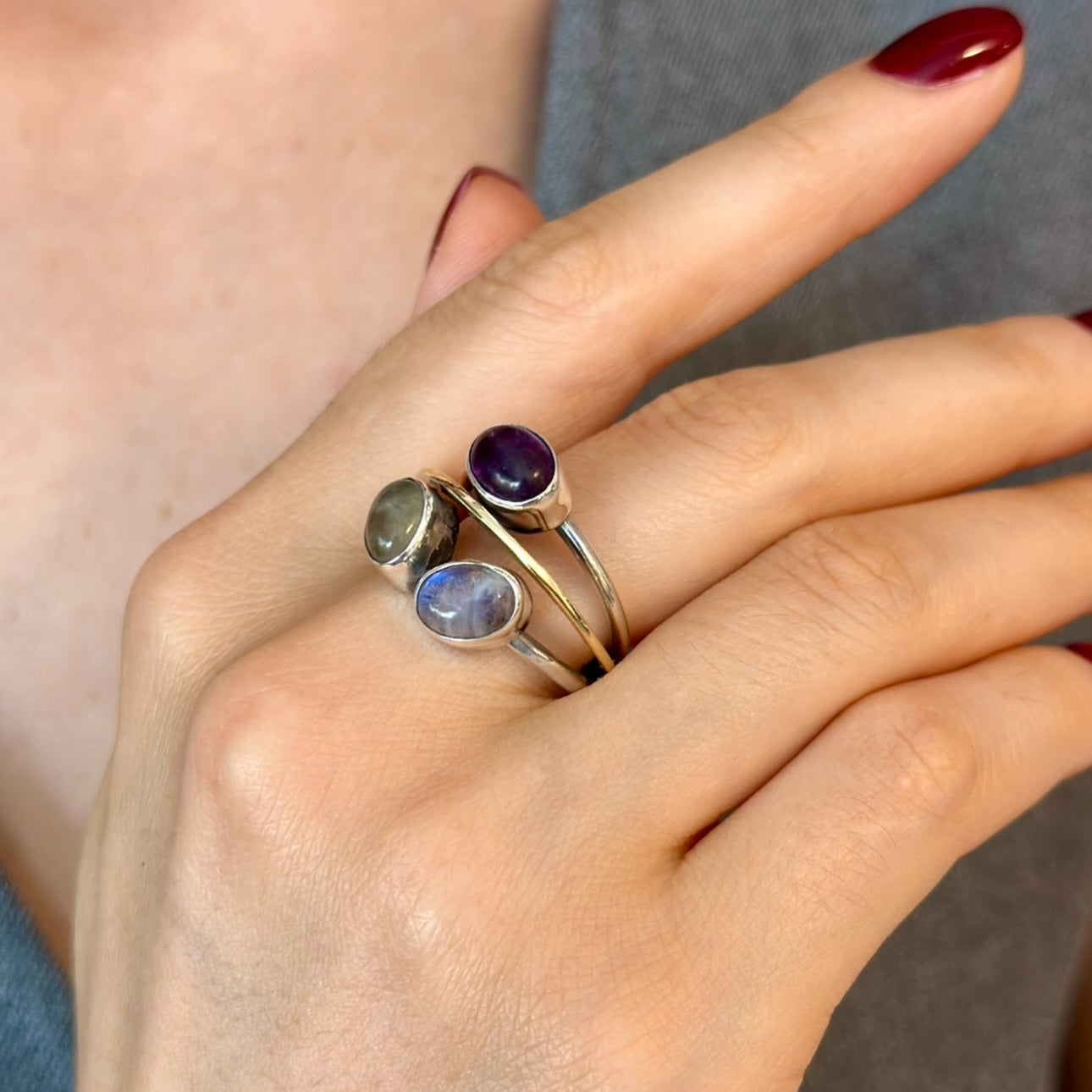 Hand wearing three gemstone rings with a neutral background