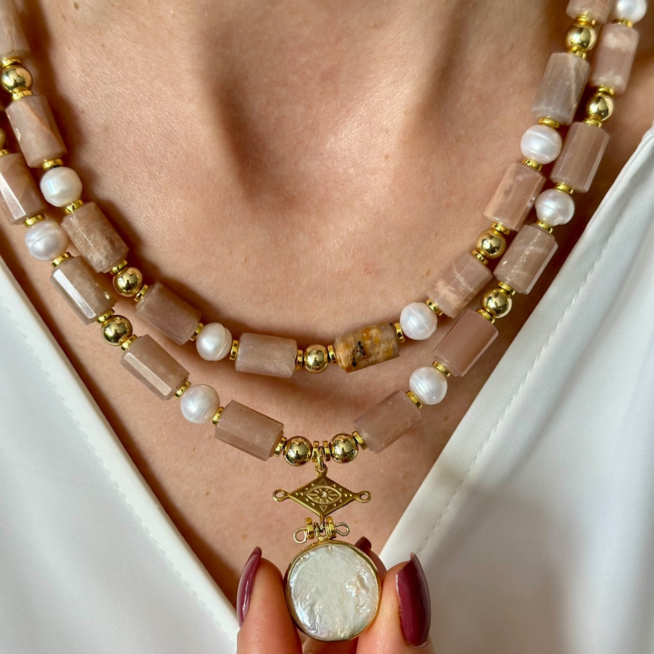 Necklace with pink beads and gold accents worn by a person against a white background