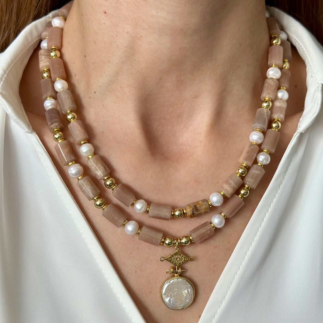 Necklace with pink beads and gold accents worn by a person against a white shirt background