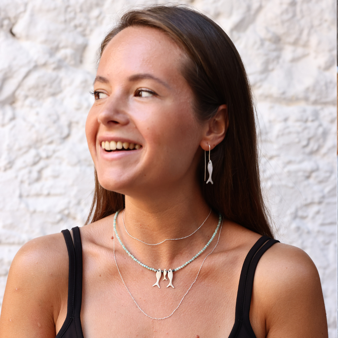 A smiling person wearing a beautiful Amazonite gemstone necklace with three fish pendants and matching earrings.