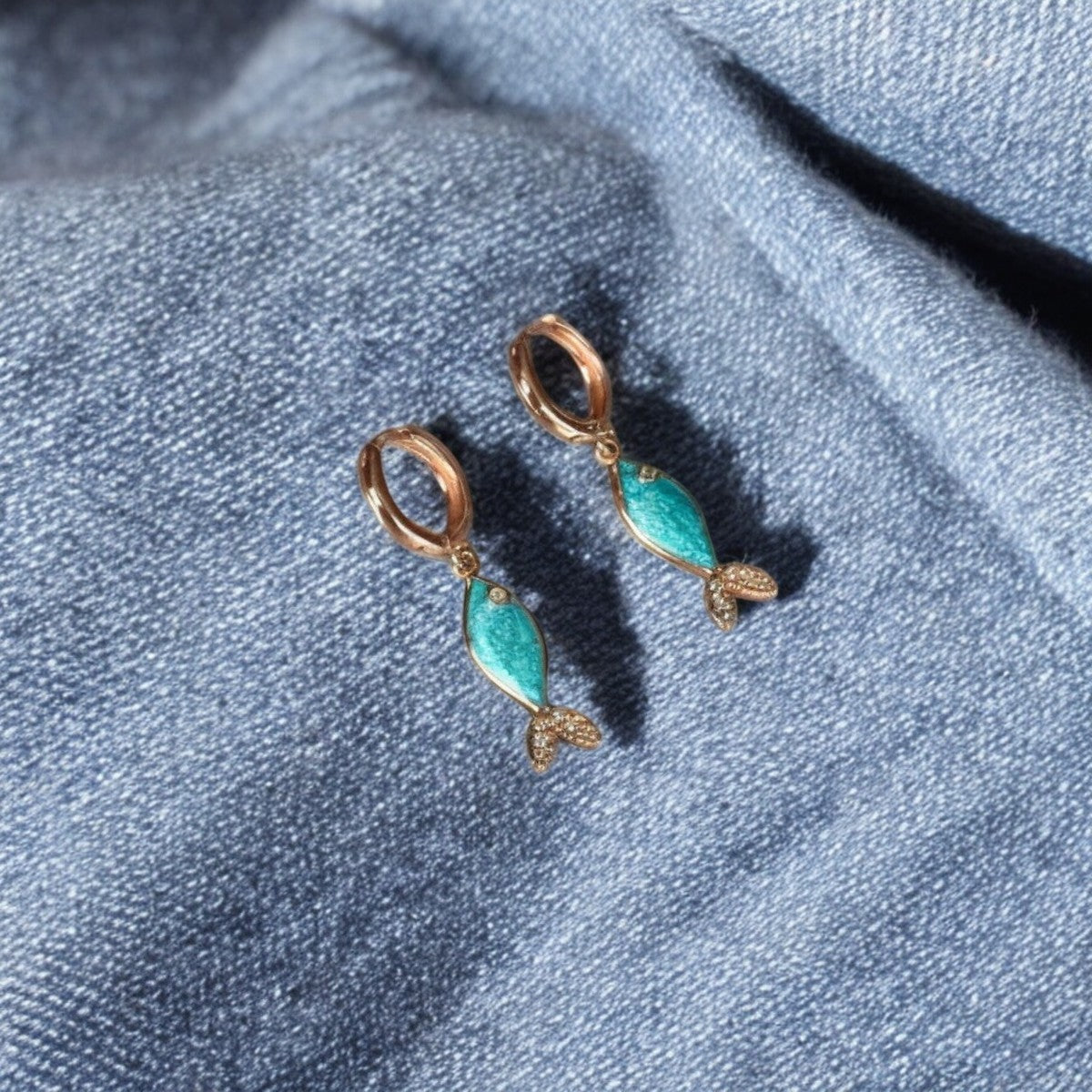 Azure fish earrings in sterling silver with rose gold plating, resting on a denim surface, showcasing handcrafted artistry.