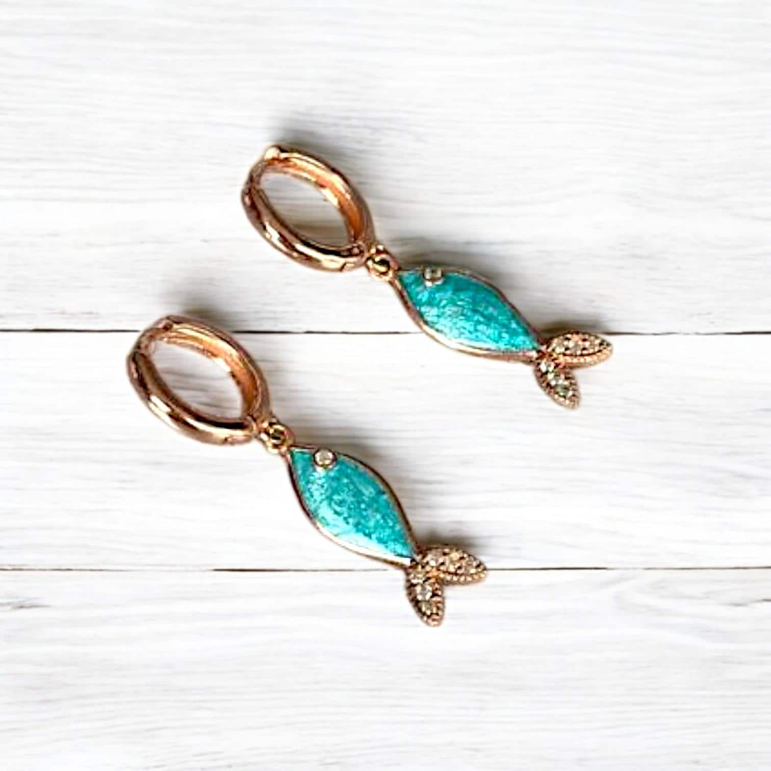Azure silver fish-shaped earrings crafted with vibrant apatite gemstones, displayed on a textured light background.