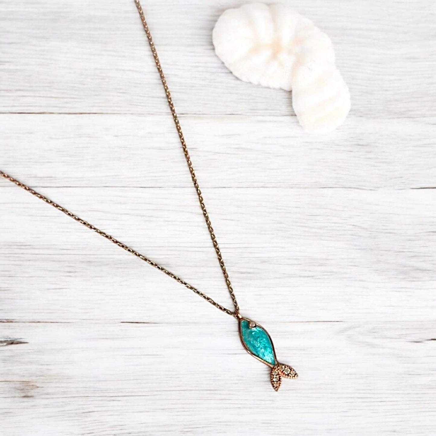 Azure blue gemstone fish necklace with silver details displayed elegantly on a light wooden background.