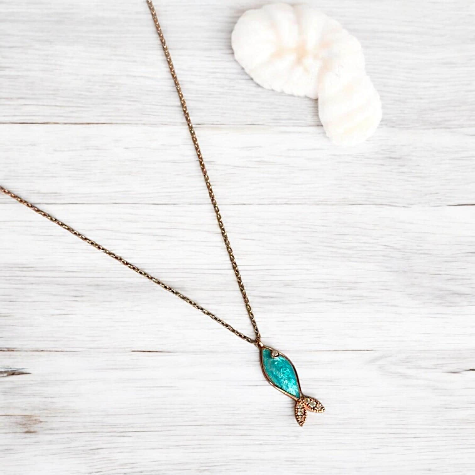 Azure blue gemstone fish necklace with silver details displayed elegantly on a light wooden background.