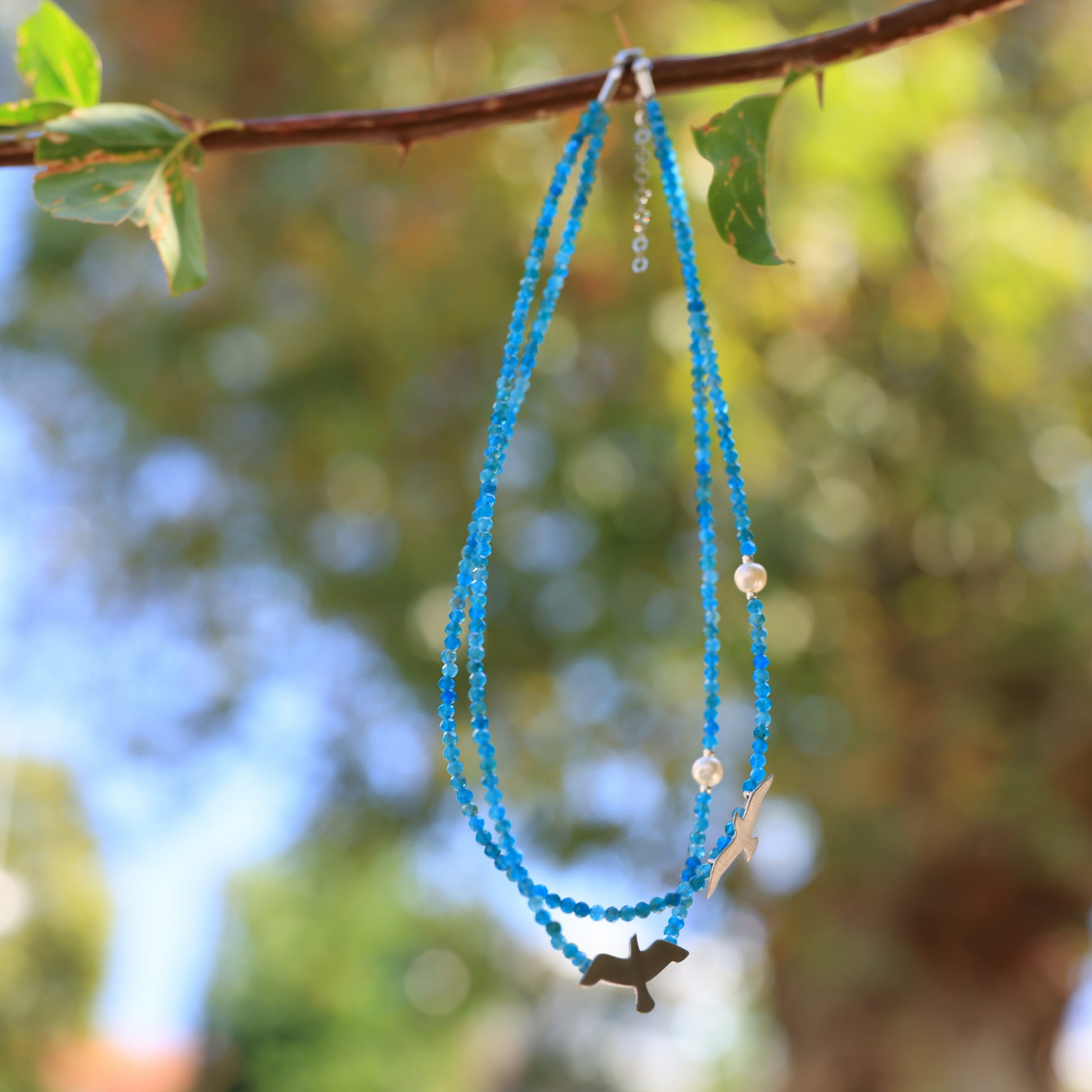 Apatite silver necklace featuring small and large seagull charms hanging elegantly outdoors with a bokeh background.