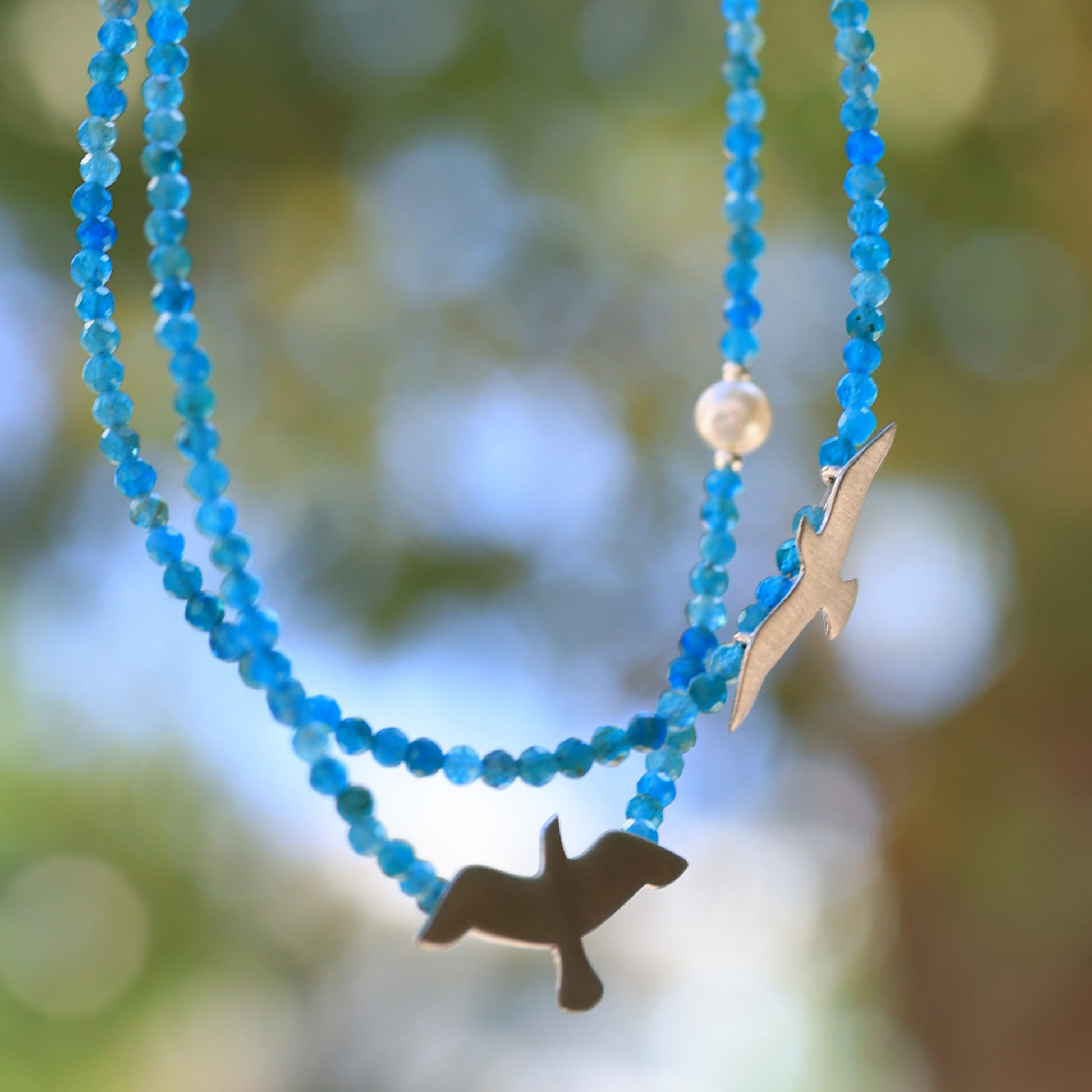 Elegant Big and Small Seagull Apatite Silver Necklace glistening against a blurred natural background.