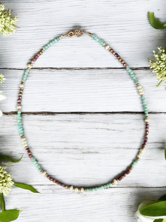 Lilith Gemstone Necklace with Lepidolite, Amazonite, and Freshwater Pearls beautifully arranged on wood with floral accents.