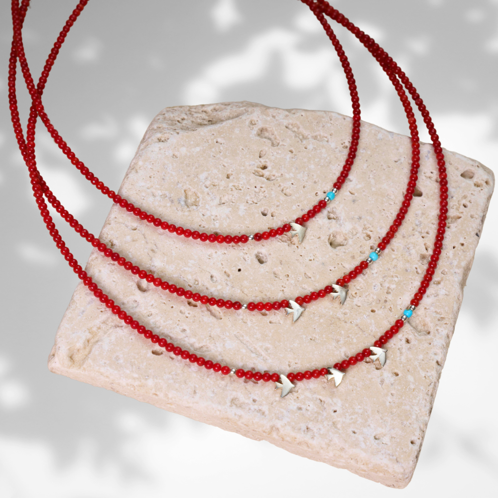 Minimalist coral gemstone necklace with 925 sterling silver bird-shaped pendants displayed on a textured stone backdrop.