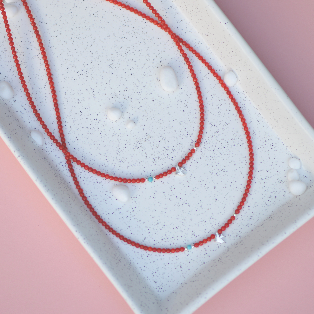 Minimalist coral gemstone necklace featuring a 925 sterling silver bird pendant, displayed on a white speckled tray.