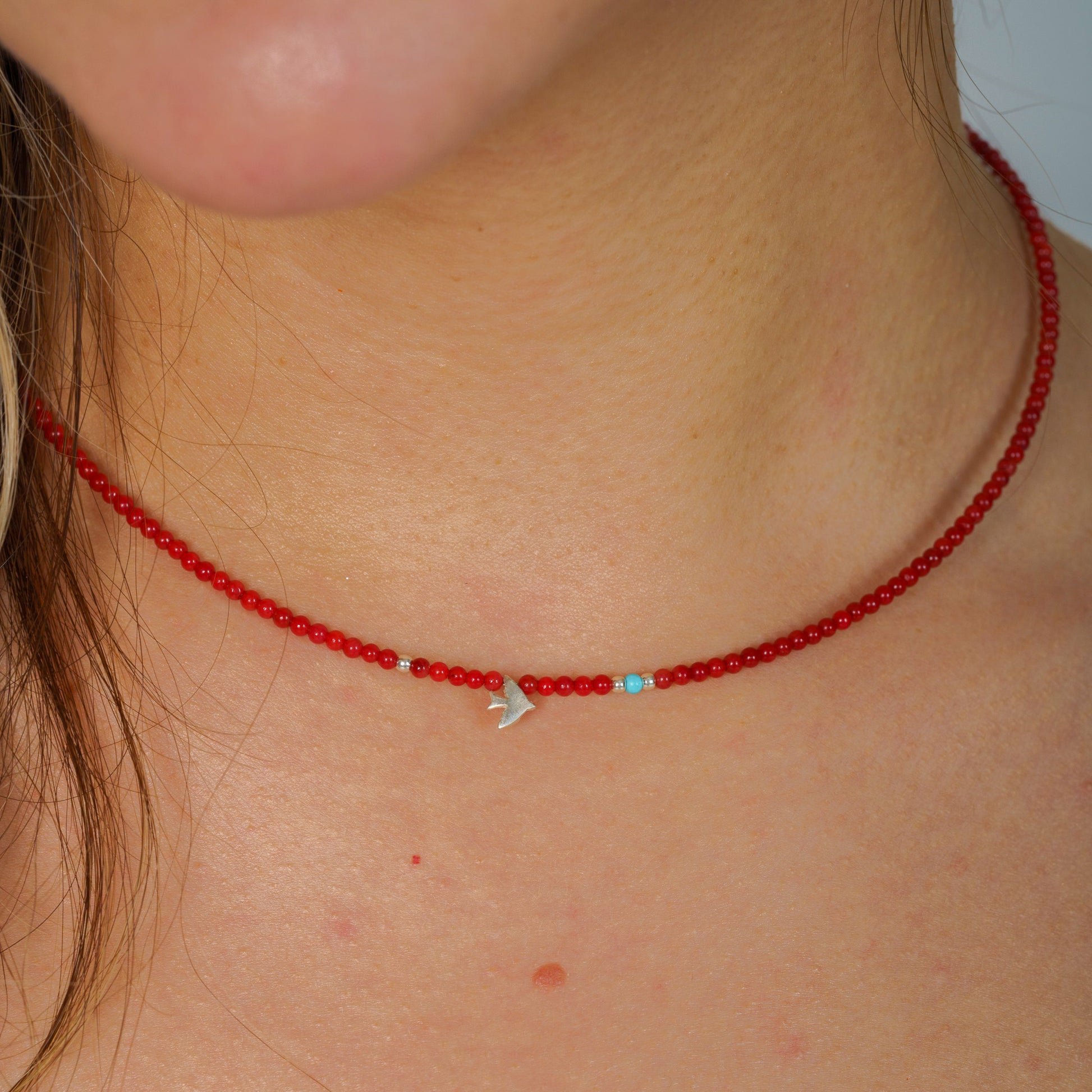 Minimalist coral gemstone necklace with a 925 sterling silver bird pendant displayed on a neck close-up view.