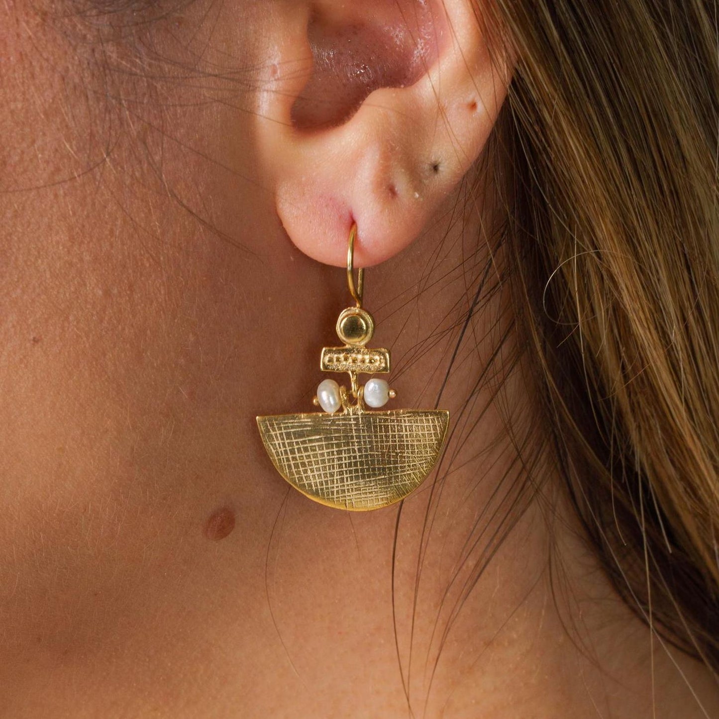Close-up of a gold-plated Selena silver earring with intricate pearl details, worn on a person's ear.