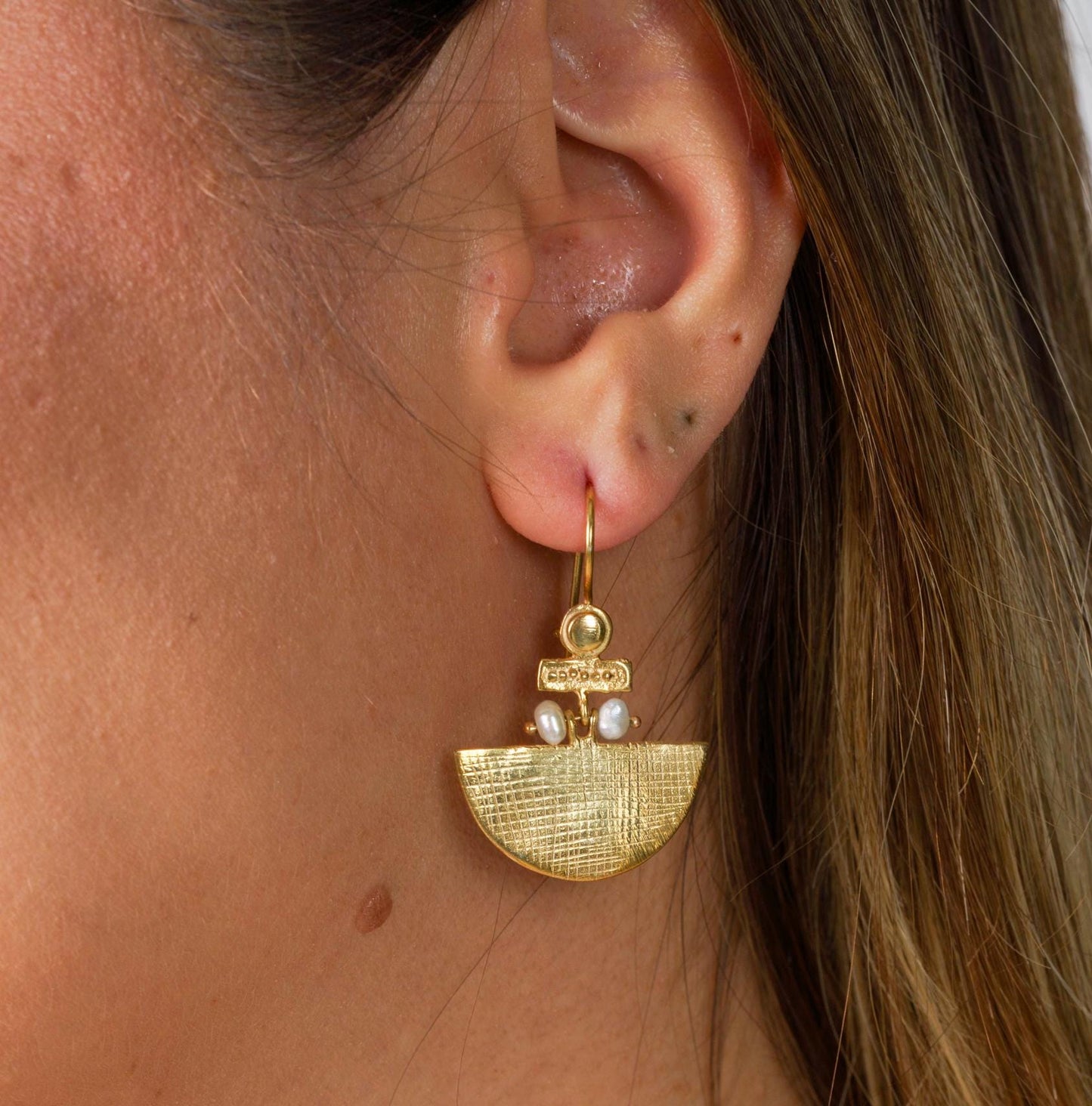 Close-up of a woman wearing Selena Silver Earrings, gold plated, featuring a textured design with pearl accents.